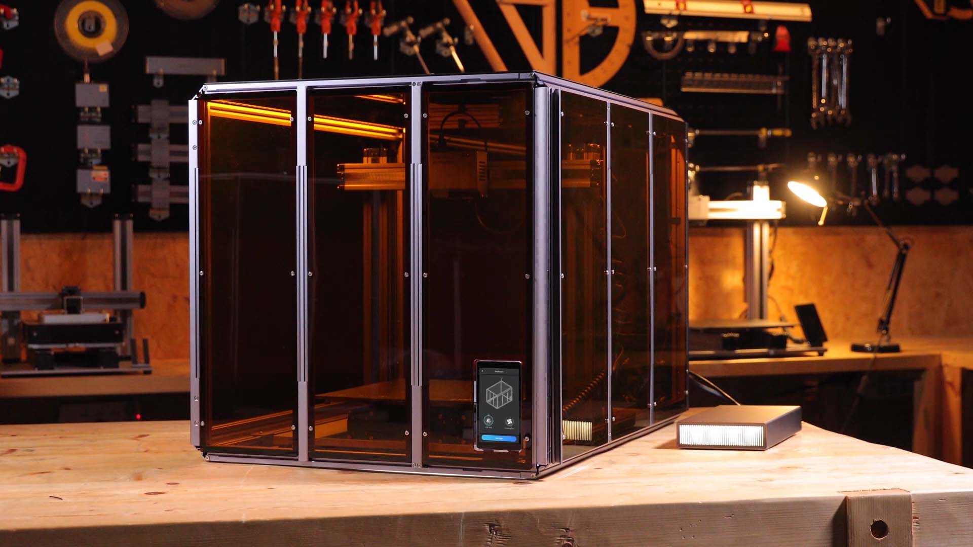Snapmaker 3-in-1 Artisan with an integrated fume extraction system on a wooden workbench. The system features a sleek, enclosed design with orange-tinted panels and a control screen, operating in a workshop with tools and a desk lamp in the background.