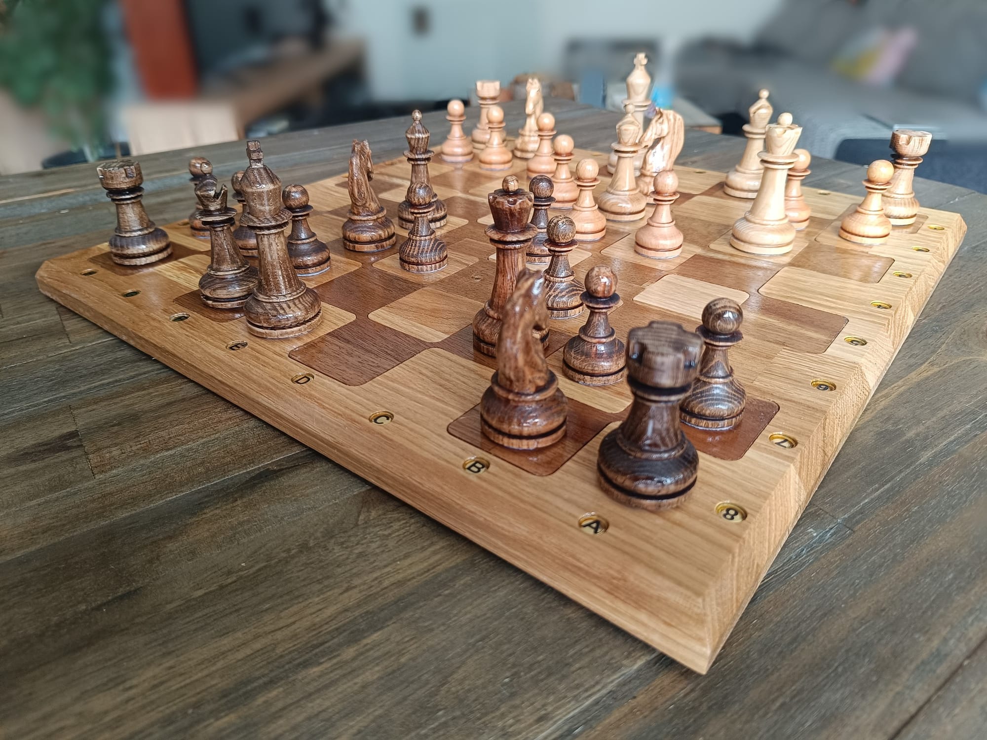 A beautifully carved wooden chessboard with a full set of geometric chess pieces sits on a table, ready for a game.