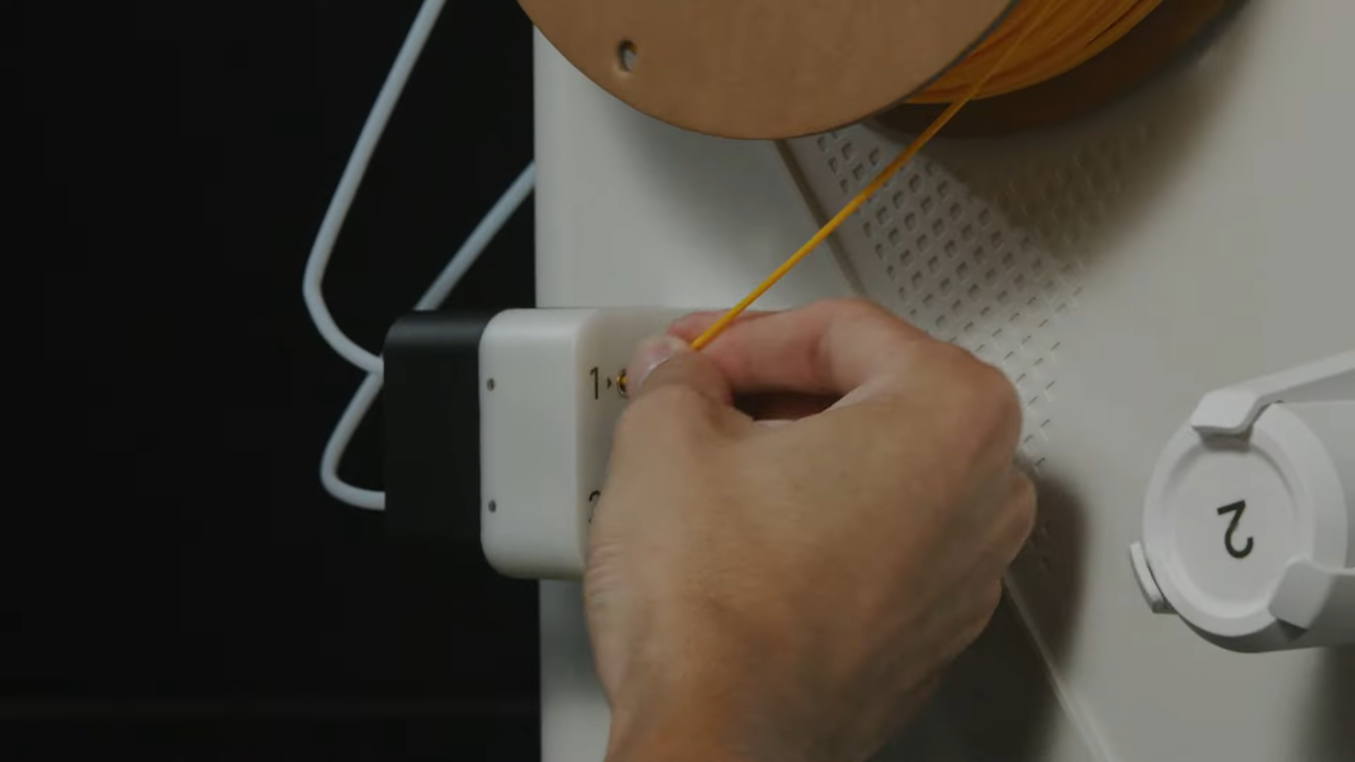 A close-up of a user guiding yellow filament into the printer's feeder mechanism to check for resistance or tangles in the filament path.