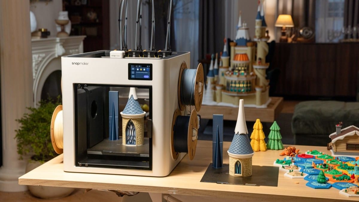A Snapmaker 3D printer with four toolheads finishing a multi-color castle tower, surrounded by completed landscape models and a large assembled castle project on a workbench.