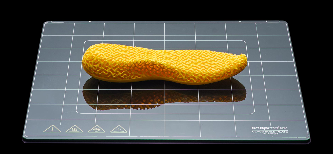 A 3D printed yellow shoe insole on a glass build plate featuring an exposed gyroid infill pattern, demonstrating how sparse internal structures save material while maintaining structural integrity.