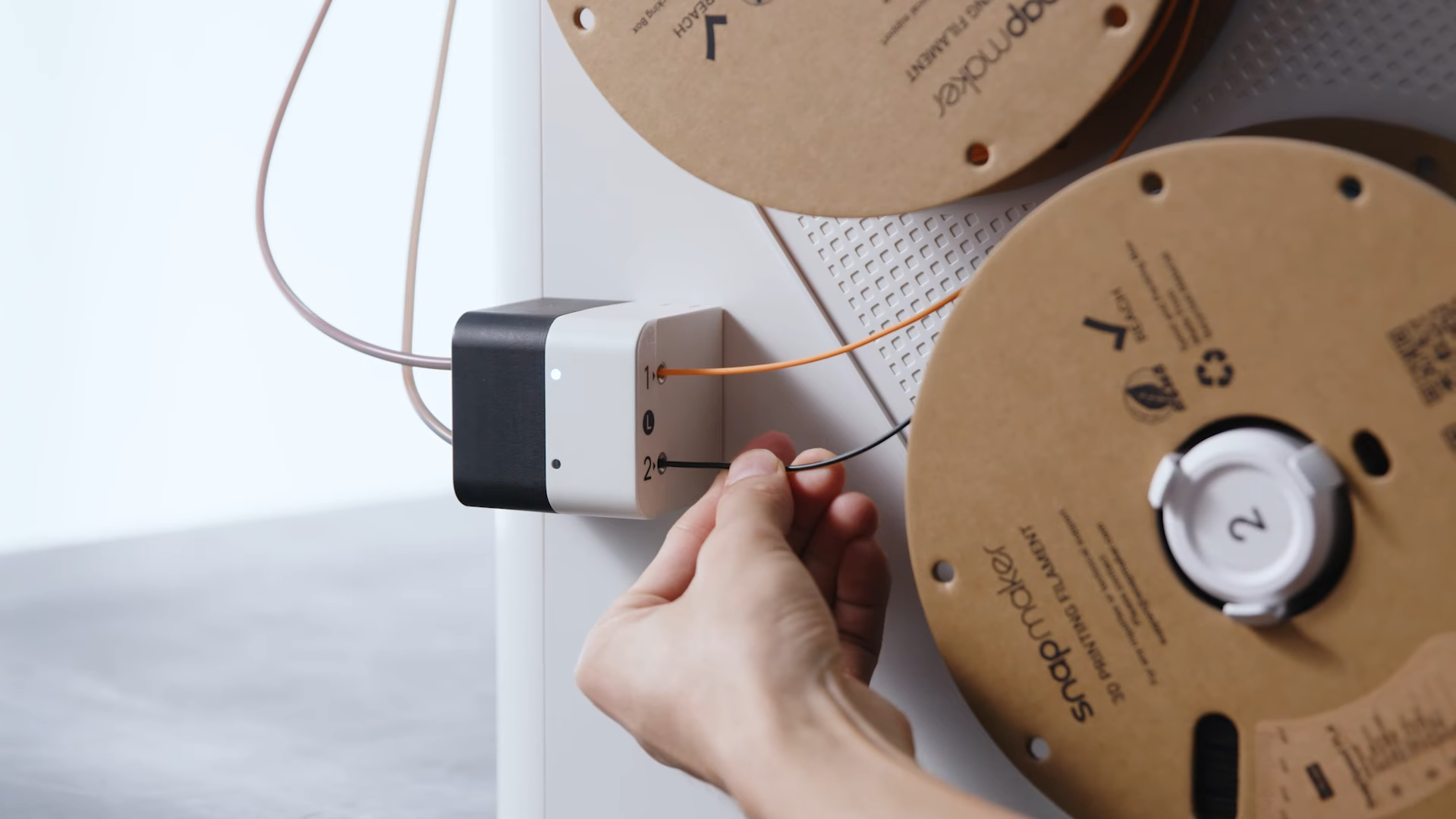 A person manually threading a piece of black 3D printing filament into a filament sensor block on a printer frame, demonstrating the setup process before printing.