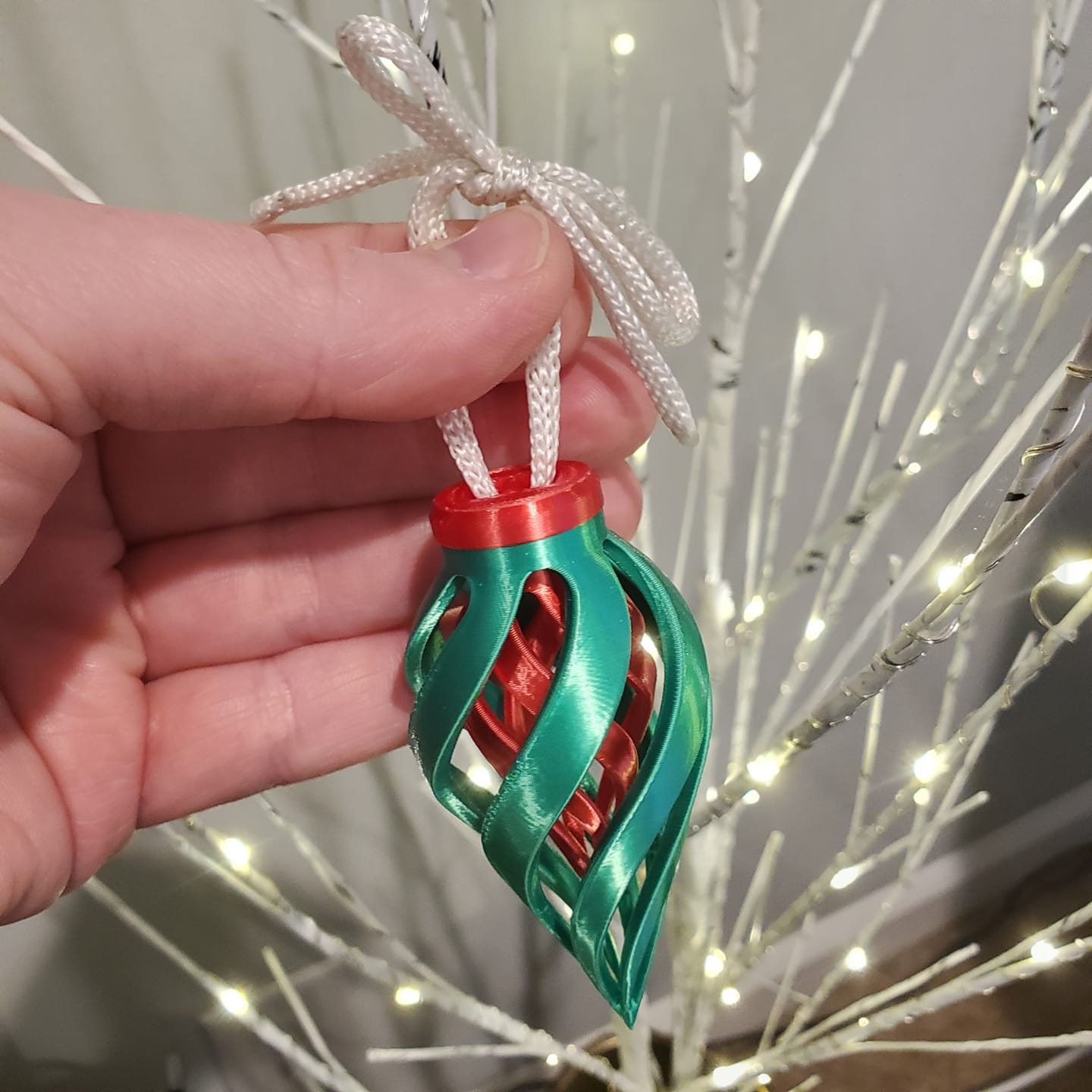 A dual-extrusion 3D printer actively creating a completely hollow, spiraled red and green Christmas ornament, showcasing material-saving vase mode printing techniques.