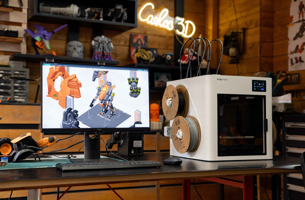 An advanced 3D printing setup in a workshop, featuring a Snapmaker multi-material printer and a monitor with slicer software for a complex project.
